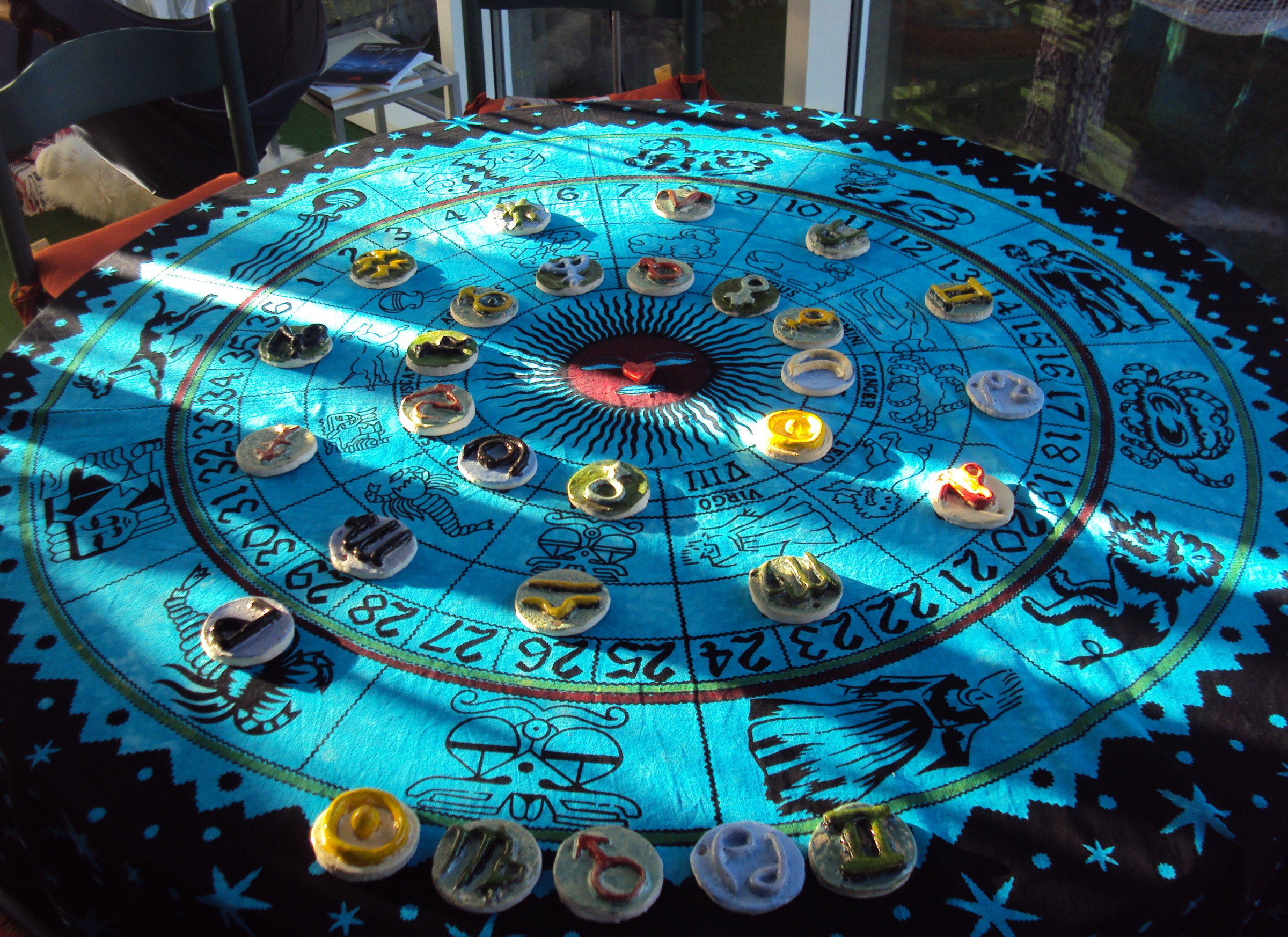 Tischtuch mit Sternenkreis und aufgelegten astrologischen Symbolen aus Ton